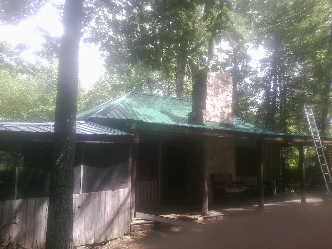 Green metal roof and stone chimney above a log cabin porch in El Segundo