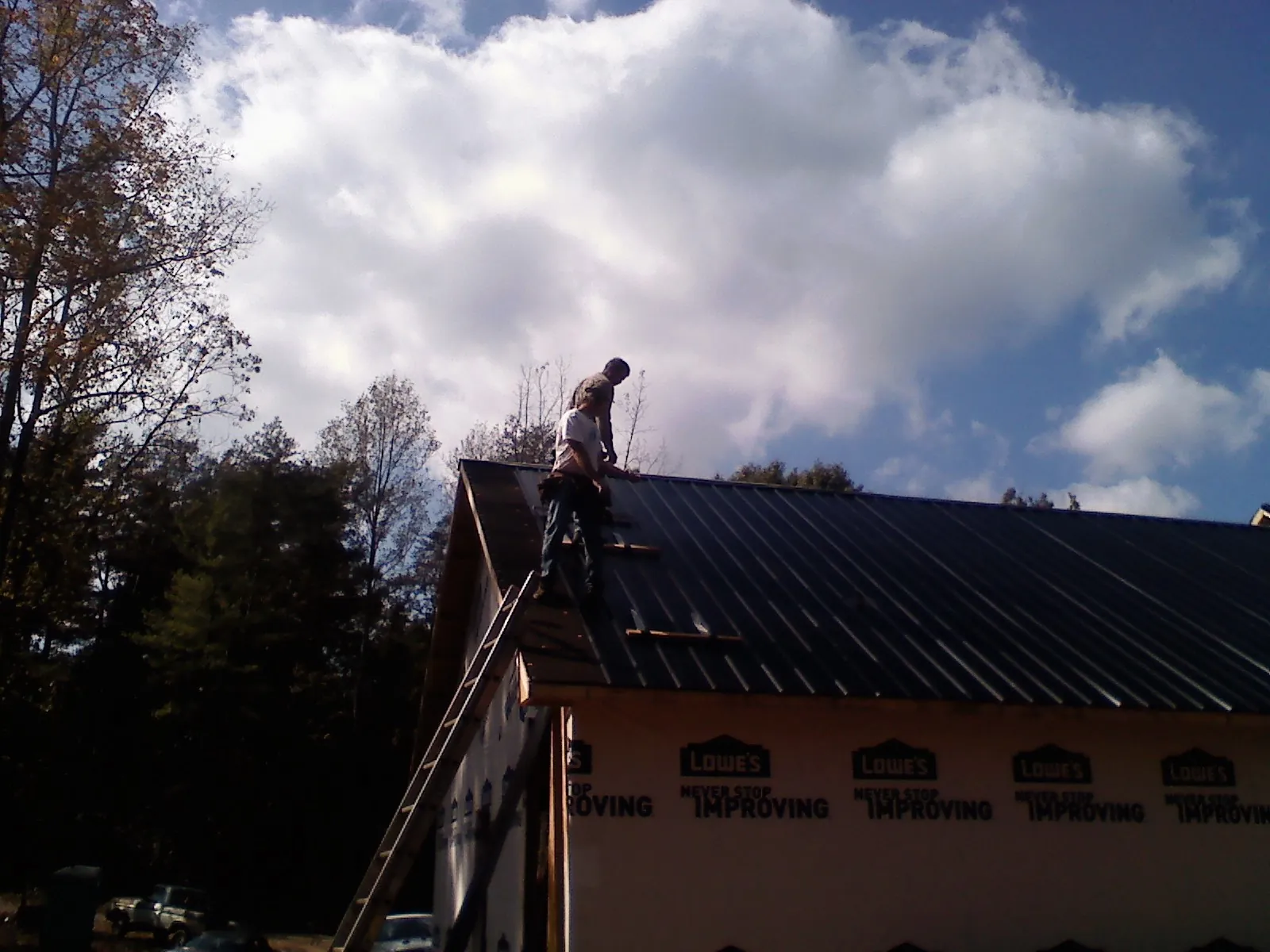 Roofer fastening dark metal panels high against a cloudy sky, from a Roof Inspection job in El Segundo